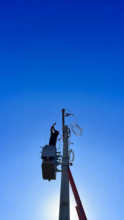 Técnico em poste de subestação contra céu azul